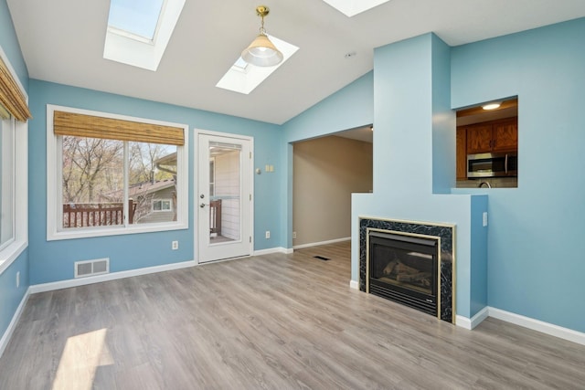 unfurnished living room with a premium fireplace, baseboards, wood finished floors, and vaulted ceiling with skylight