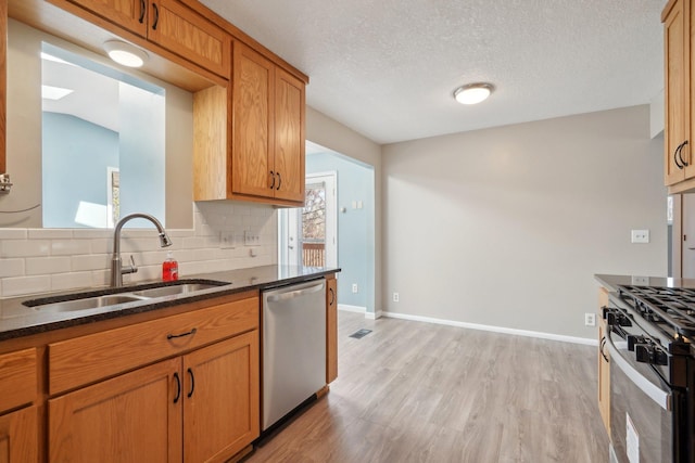 kitchen featuring range with gas cooktop, backsplash, stainless steel dishwasher, a sink, and light wood finished floors