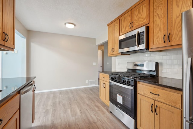kitchen featuring visible vents, appliances with stainless steel finishes, tasteful backsplash, light wood-type flooring, and dark stone countertops