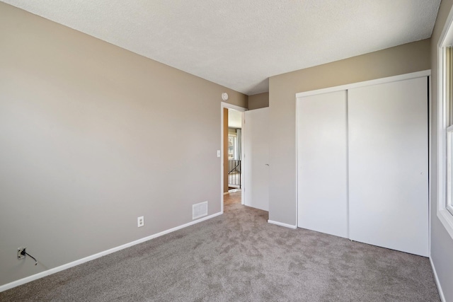 unfurnished bedroom featuring carpet flooring, a textured ceiling, baseboards, visible vents, and a closet