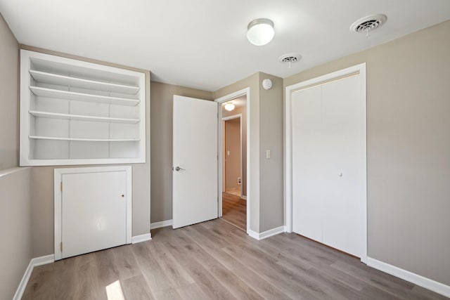 unfurnished bedroom featuring baseboards, a closet, wood finished floors, and visible vents