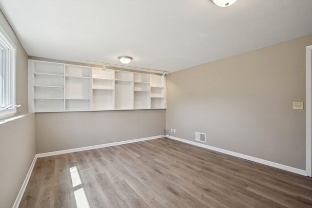 spare room with baseboards, visible vents, and wood finished floors