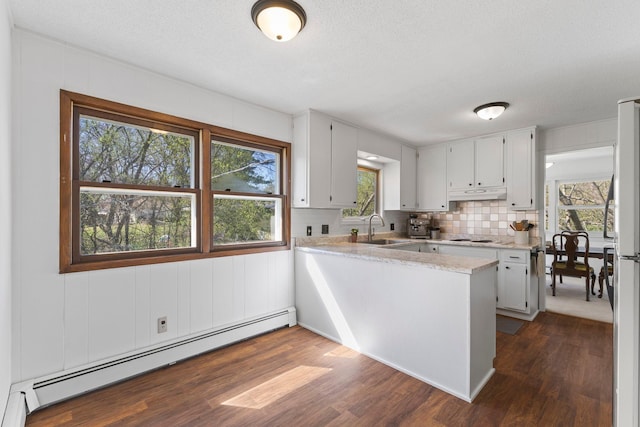 kitchen featuring a sink, a baseboard radiator, a peninsula, under cabinet range hood, and dark wood-type flooring
