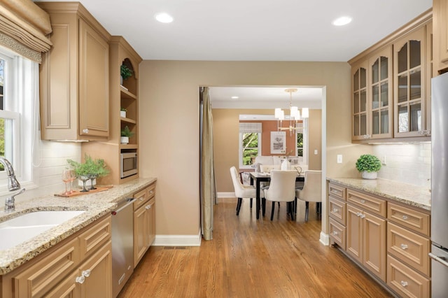 kitchen with decorative backsplash, glass insert cabinets, a sink, light wood finished floors, and stainless steel appliances