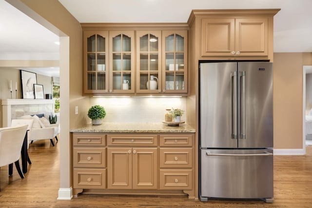 kitchen with high end fridge, light stone counters, wood finished floors, and tasteful backsplash