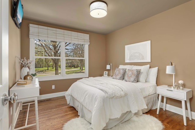 bedroom with baseboards, wood finished floors, and visible vents