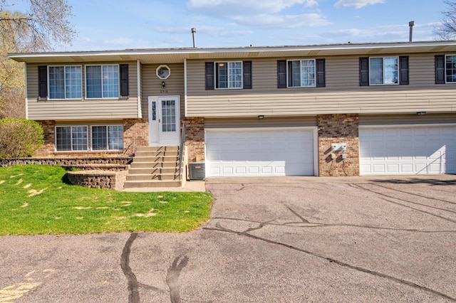 split foyer home with brick siding, aphalt driveway, central AC unit, and a garage
