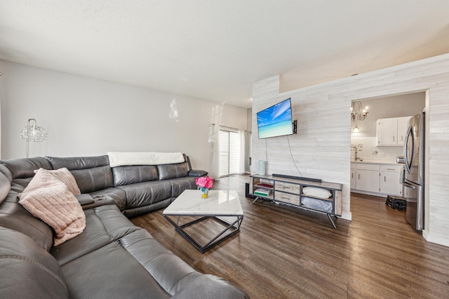 living room featuring an inviting chandelier, wood walls, and dark wood finished floors