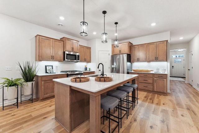 kitchen with brown cabinets, a breakfast bar, a sink, light wood-style flooring, and stainless steel appliances