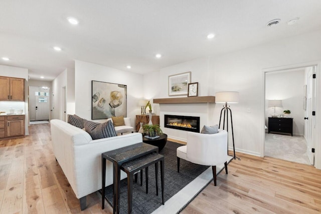 living area with recessed lighting, a glass covered fireplace, and light wood finished floors