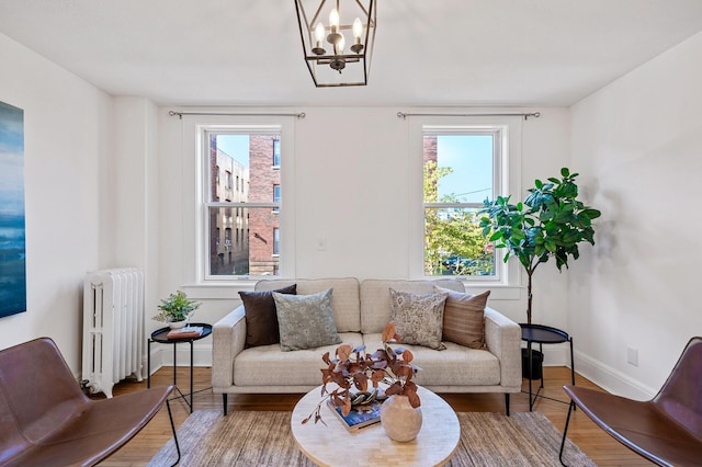 living area featuring wood finished floors, baseboards, radiator heating unit, and a notable chandelier