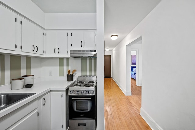 kitchen with light wood finished floors, electric range oven, light countertops, white cabinetry, and under cabinet range hood