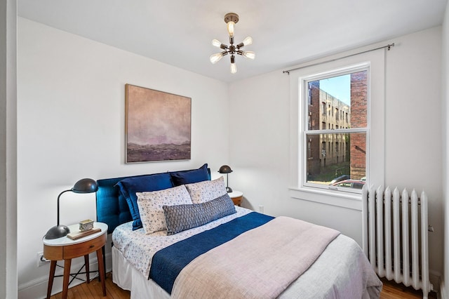 bedroom with wood finished floors, baseboards, radiator heating unit, and a chandelier