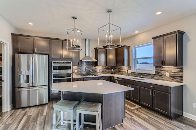 kitchen featuring stainless steel appliances, dark brown cabinetry, a sink, and wall chimney exhaust hood