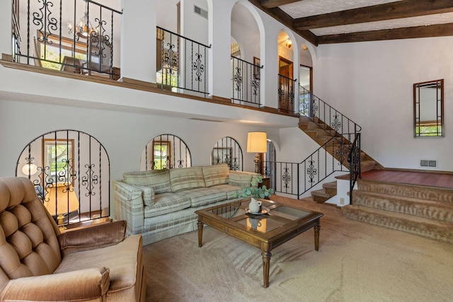 carpeted living area featuring a towering ceiling, stairs, beam ceiling, and arched walkways