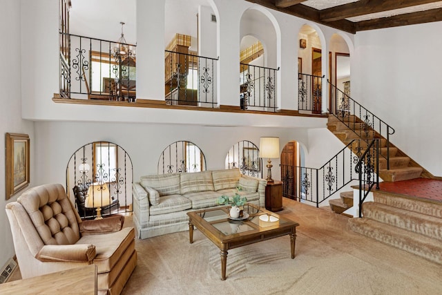 carpeted living room with a towering ceiling, arched walkways, beamed ceiling, stairway, and a chandelier