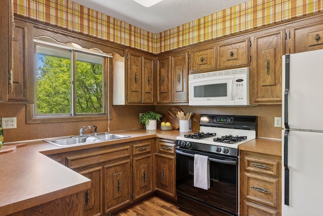 kitchen with white appliances, a sink, wallpapered walls, brown cabinetry, and a textured ceiling