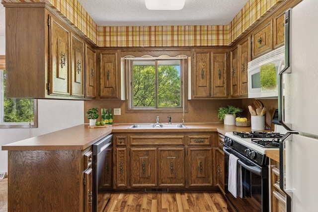 kitchen featuring white appliances, a sink, light wood-style floors, a textured ceiling, and brown cabinetry