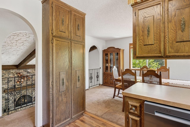 kitchen featuring stainless steel dishwasher, a textured ceiling, light countertops, brown cabinetry, and arched walkways