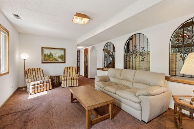 carpeted living area with arched walkways, a textured ceiling, and baseboards