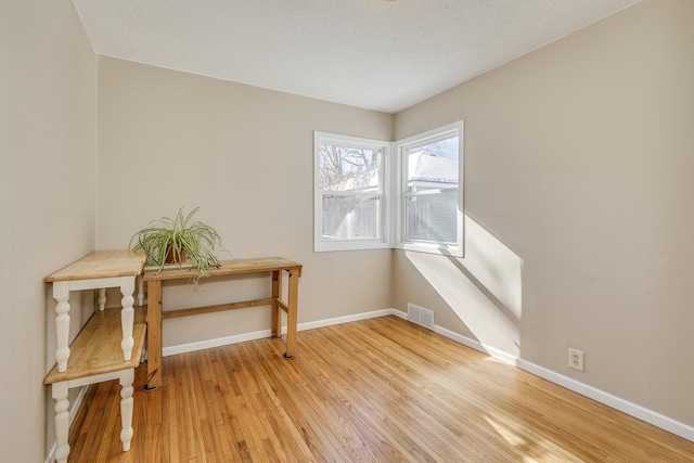 empty room with light wood finished floors, a textured ceiling, visible vents, and baseboards