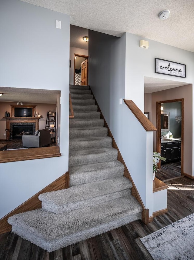 19288 Evenston Dr, Farmington, MN 55024 - stairs featuring wood finished floors, a textured ceiling, a fireplace, and baseboards