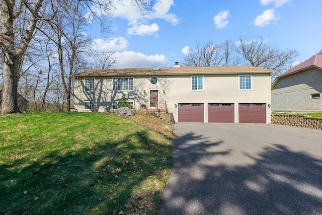 raised ranch with a garage, a chimney, a front lawn, and aphalt driveway