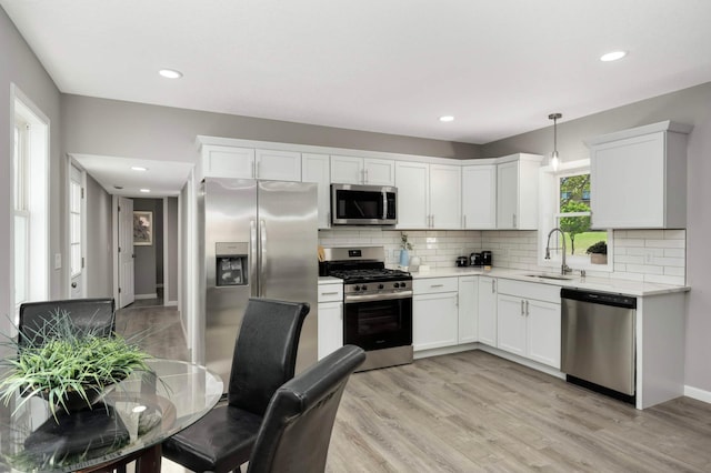kitchen featuring appliances with stainless steel finishes, a sink, decorative backsplash, light countertops, and light wood-style flooring