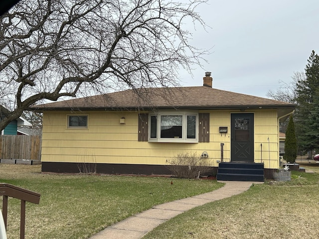 view of front facade featuring a chimney, roof with shingles, a front lawn, and fence