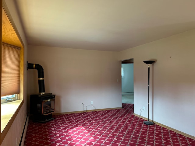 empty room with a wood stove, dark colored carpet, baseboards, and a baseboard radiator