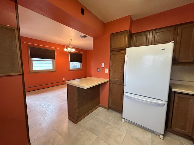 kitchen featuring a peninsula, freestanding refrigerator, decorative light fixtures, light countertops, and a notable chandelier
