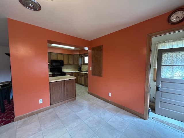 kitchen featuring light countertops, baseboards, black appliances, and a sink