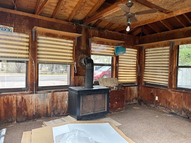 interior space featuring a ceiling fan, carpet, wooden walls, and a wood stove
