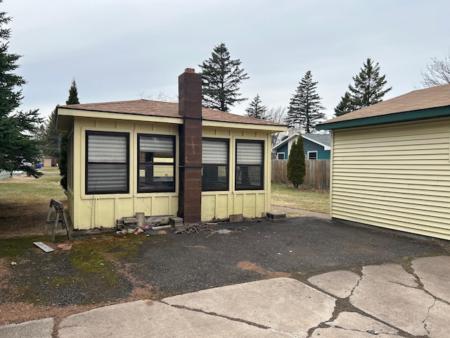 rear view of property with a chimney, board and batten siding, roof with shingles, and fence