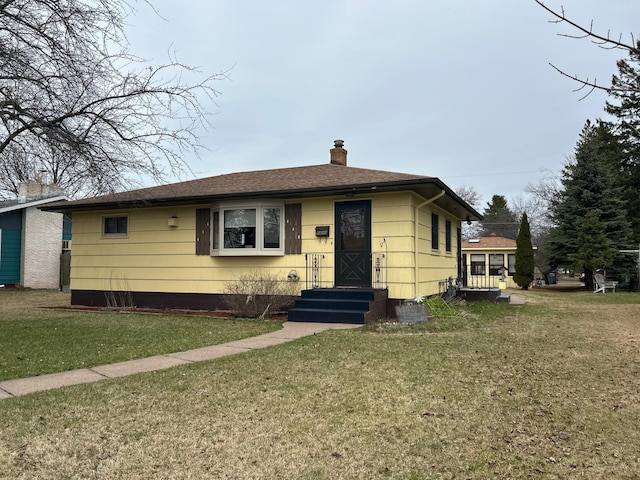 view of front of home with a shingled roof, a front lawn, and a chimney