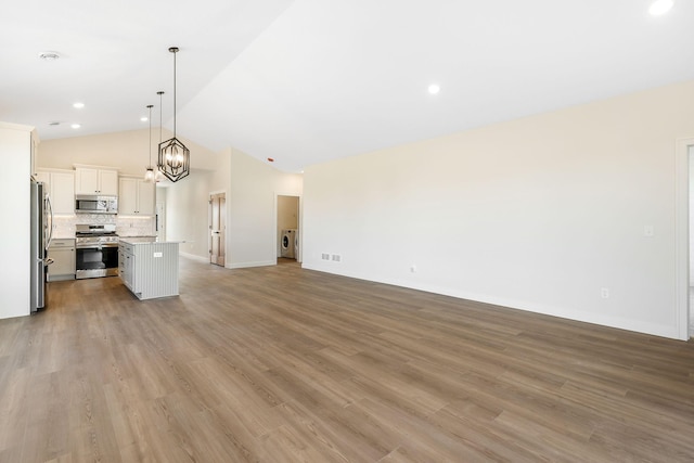 25882 Emerson Ct, Wyoming, MN 55092 - unfurnished living room featuring light wood finished floors, washing machine and dryer, vaulted ceiling, and baseboards