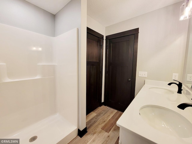 full bathroom with double vanity, a shower stall, a sink, and wood finished floors