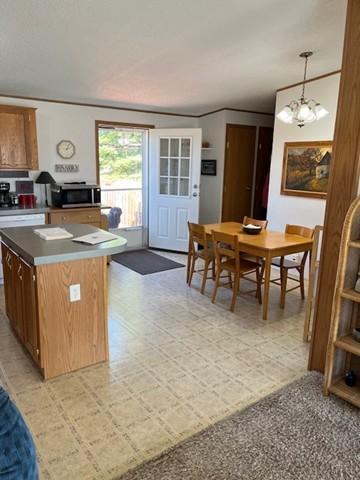 kitchen featuring a kitchen island, light floors, stainless steel microwave, brown cabinets, and decorative light fixtures