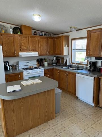 kitchen with brown cabinetry, a textured ceiling, a sink, under cabinet range hood, and white appliances