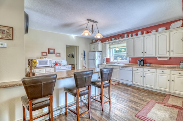 kitchen featuring white appliances, white cabinetry, a breakfast bar, and a sink