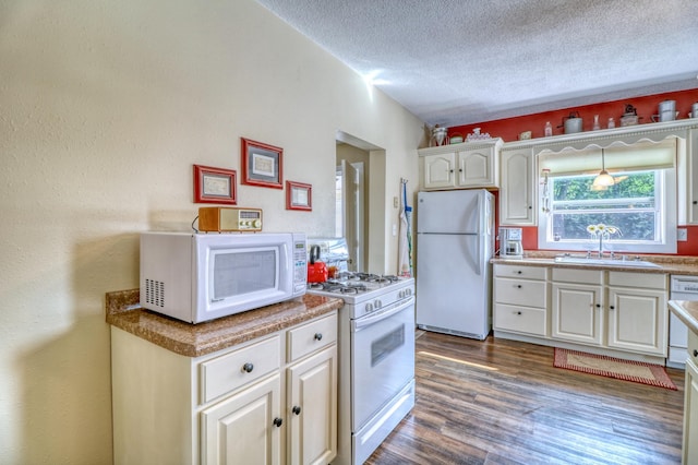 kitchen featuring a textured ceiling, dark wood finished floors, a sink, white appliances, and white cabinetry