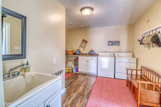 clothes washing area featuring a textured ceiling, dark wood finished floors, cabinet space, a sink, and washer and dryer