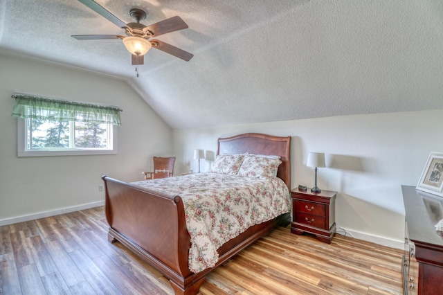 bedroom featuring wood finished floors, baseboards, a textured ceiling, and lofted ceiling