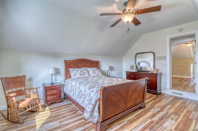 bedroom with ceiling fan, light wood finished floors, a textured ceiling, baseboards, and lofted ceiling