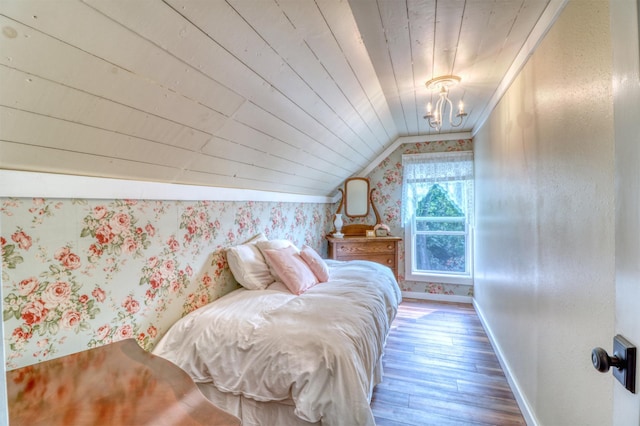 bedroom featuring wood-type flooring, an inviting chandelier, baseboards, wallpapered walls, and vaulted ceiling