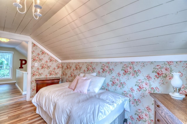 bedroom with lofted ceiling, light wood-style floors, baseboards, wallpapered walls, and a chandelier