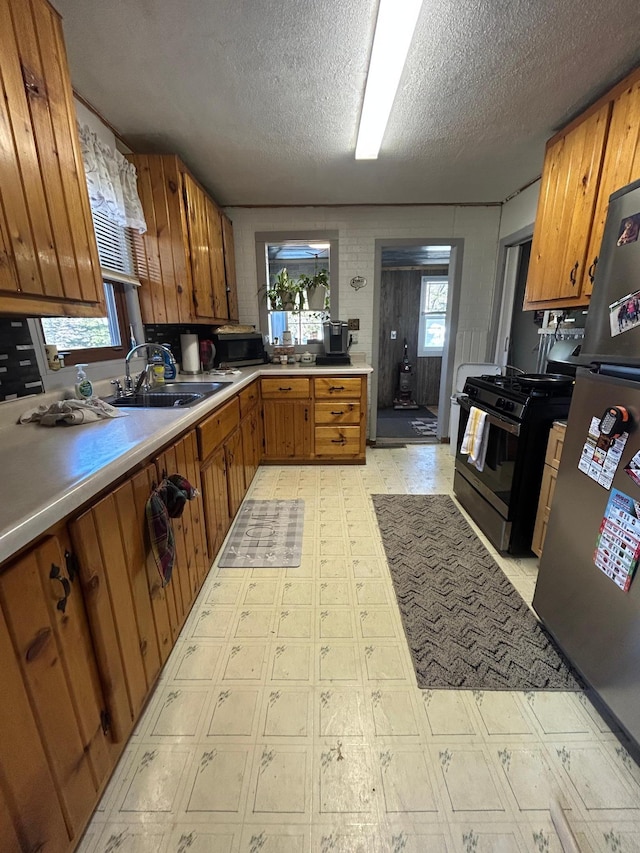 kitchen featuring brown cabinetry, a sink, light floors, and appliances with stainless steel finishes