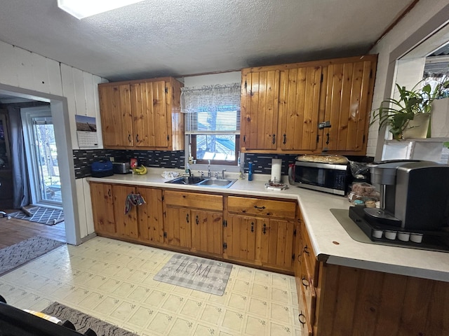 kitchen with a sink, stainless steel microwave, tasteful backsplash, and light countertops
