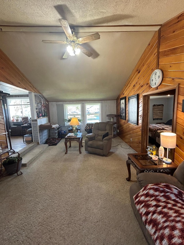 living area featuring carpet floors, wood walls, a textured ceiling, a ceiling fan, and vaulted ceiling