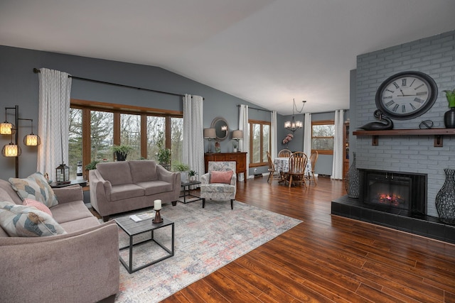living room featuring vaulted ceiling, wood finished floors, a chandelier, and a brick fireplace
